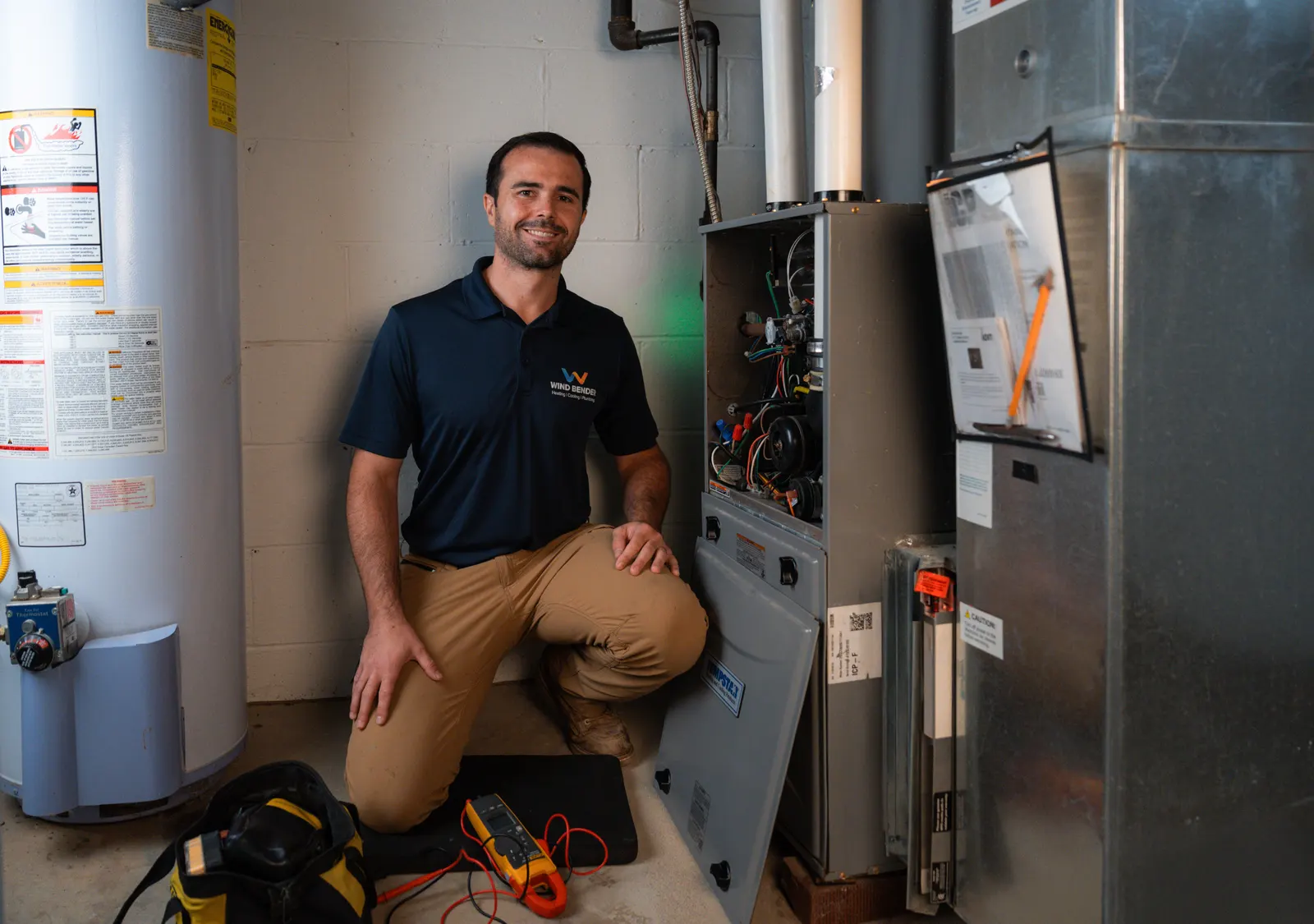 A Wind Bender technician kneeling beside an open furnace in a basement