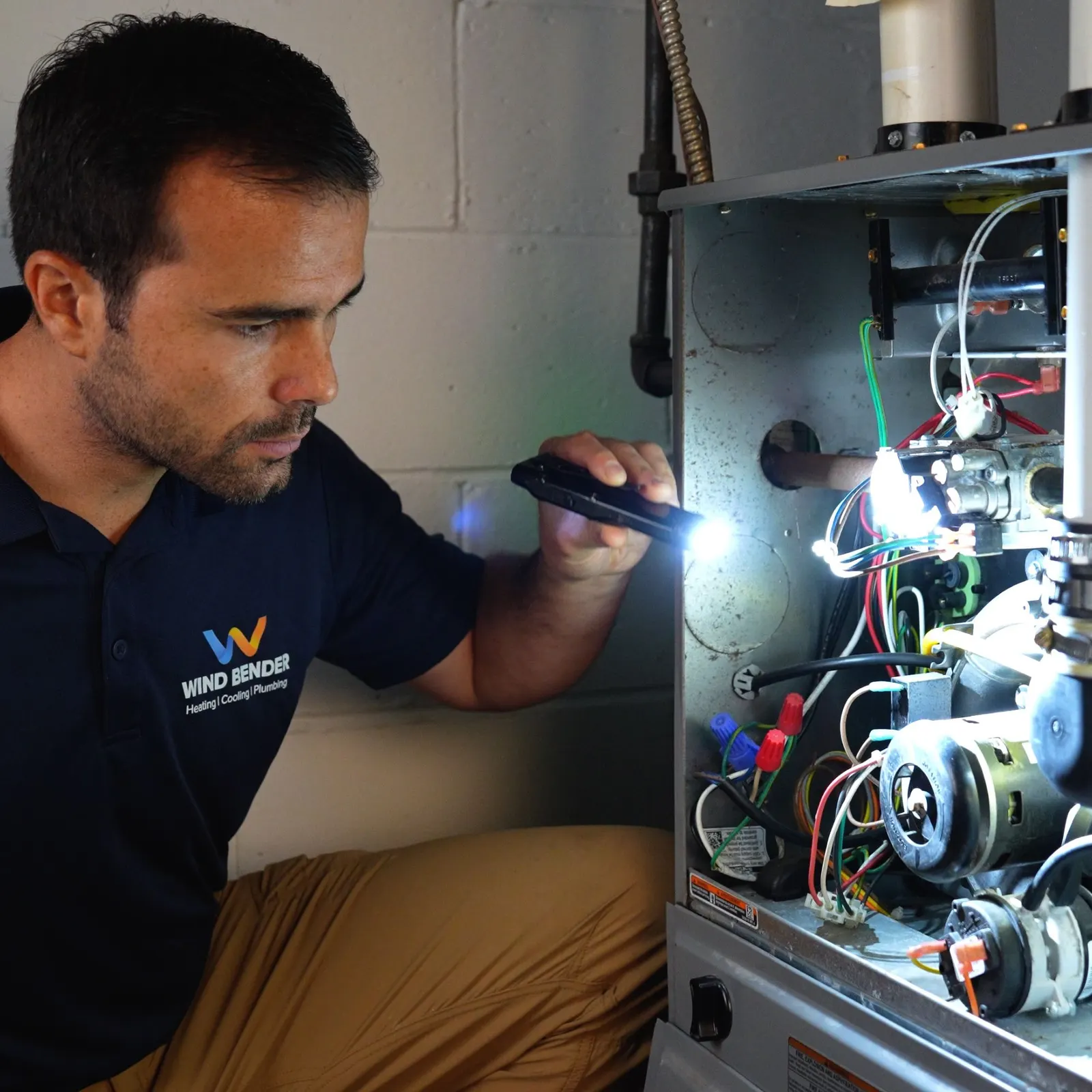 A Wind Bender technician inspecting the inside of a furnace with a flashlight